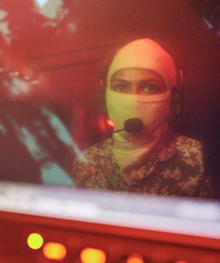 Sailor operating touchscreens under red lighting in a ship's command control room.